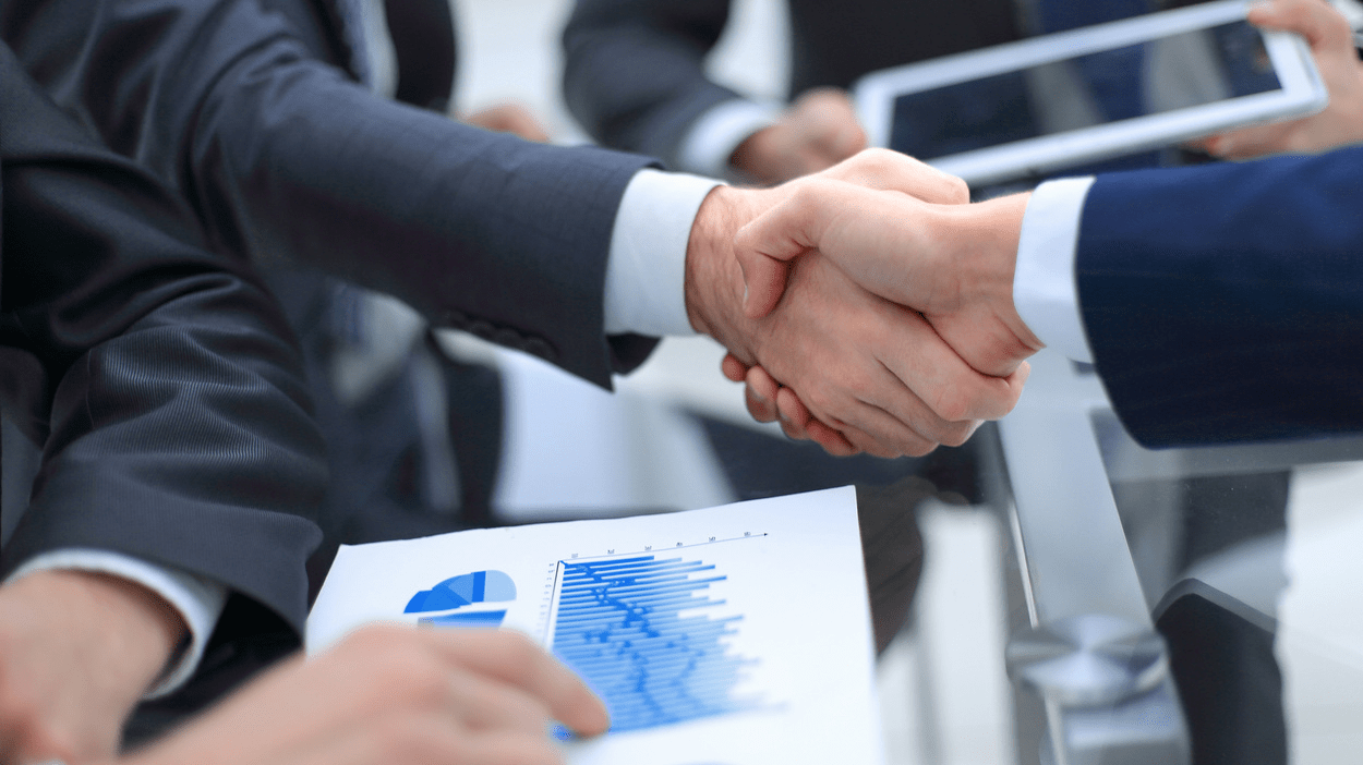 Personer gir håndtrykk mens andre peker på grafer.